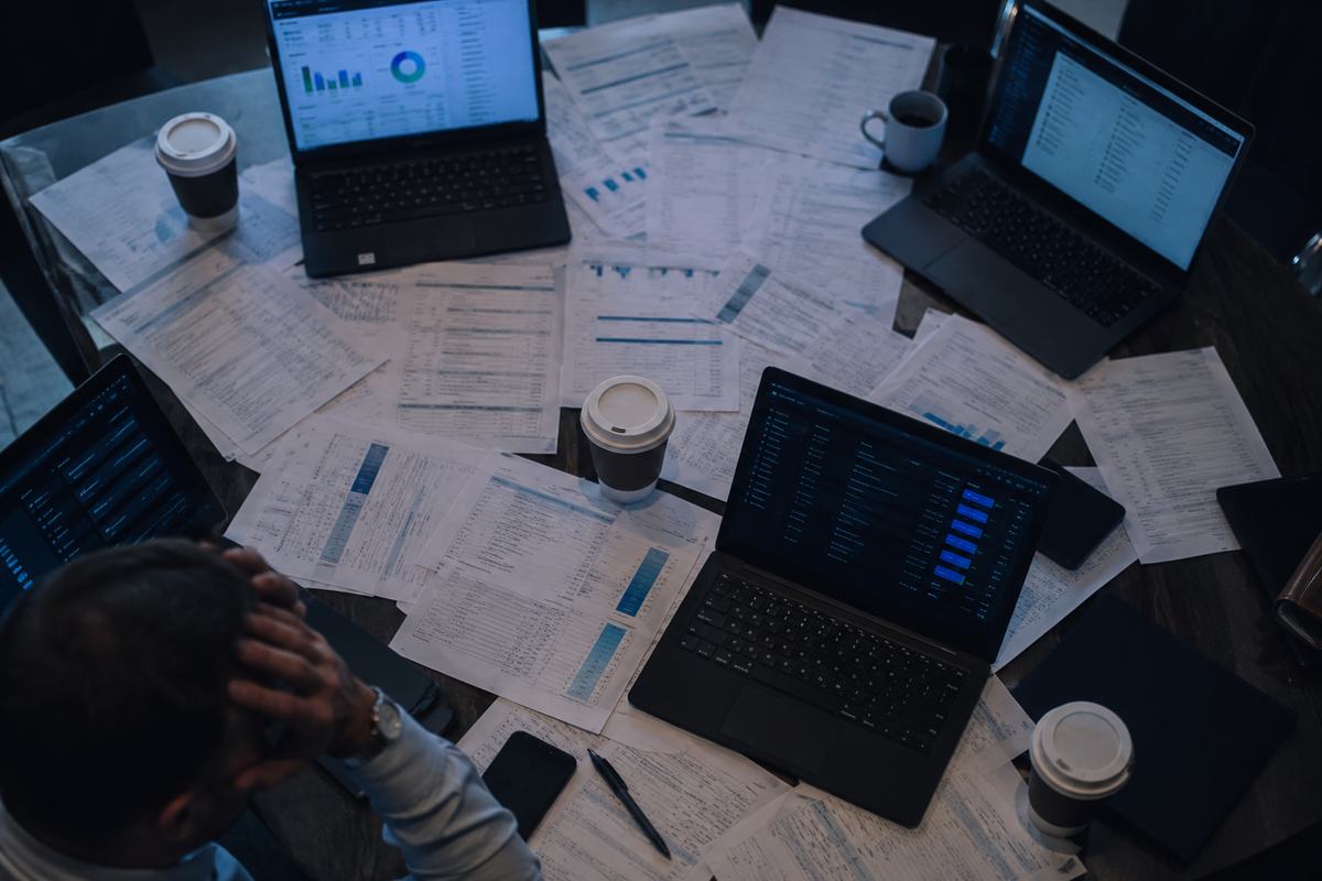 A conference table buried in printed vendor quotes and laptops showing competing pricing dashboards